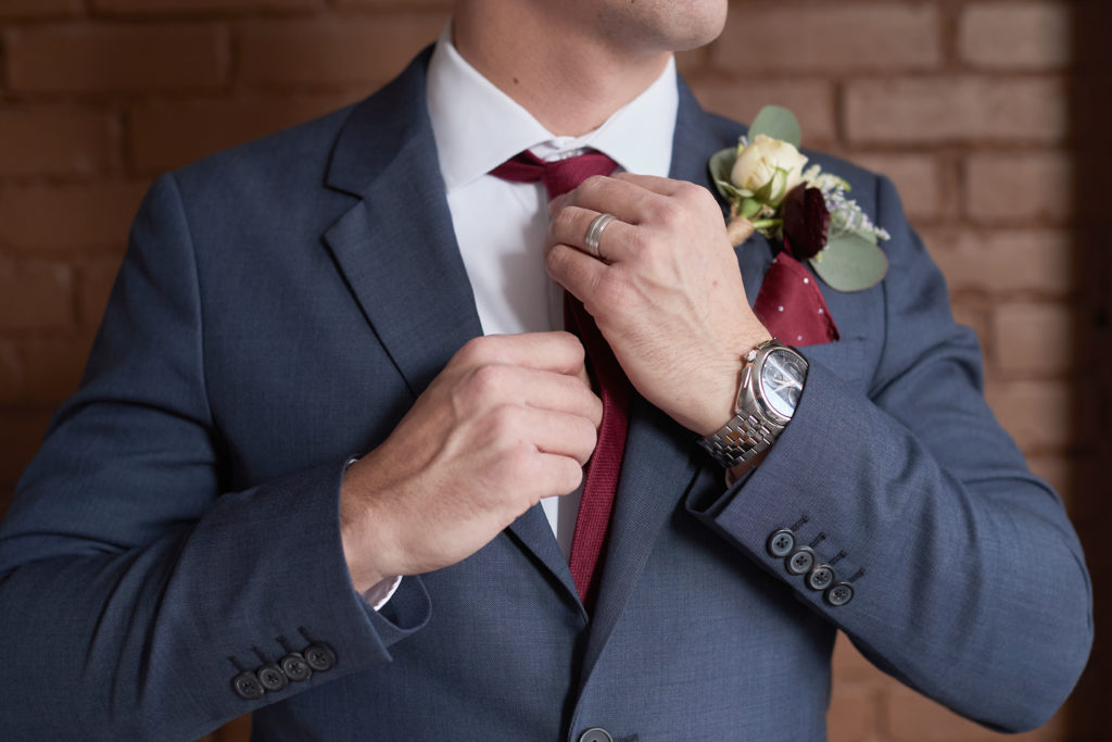 Groom adjusting his burgundy tie on wedding day. Photo by Vanessa Joy Photography