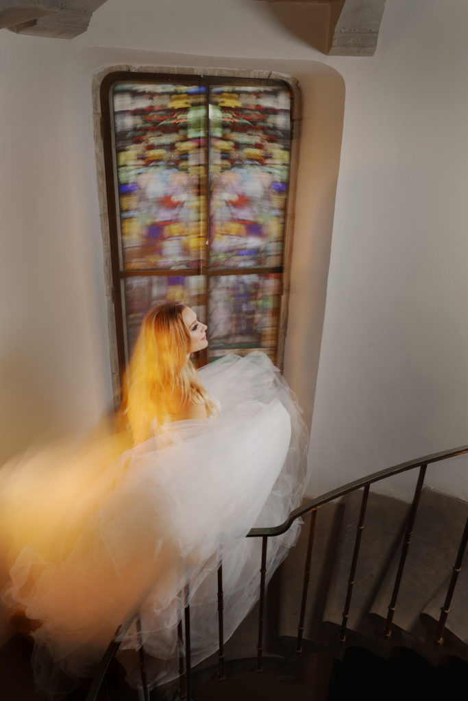 slow shutter speed blurry photo of bride going up the stairs by stained glass window. Photo by Vanessa Joy photography