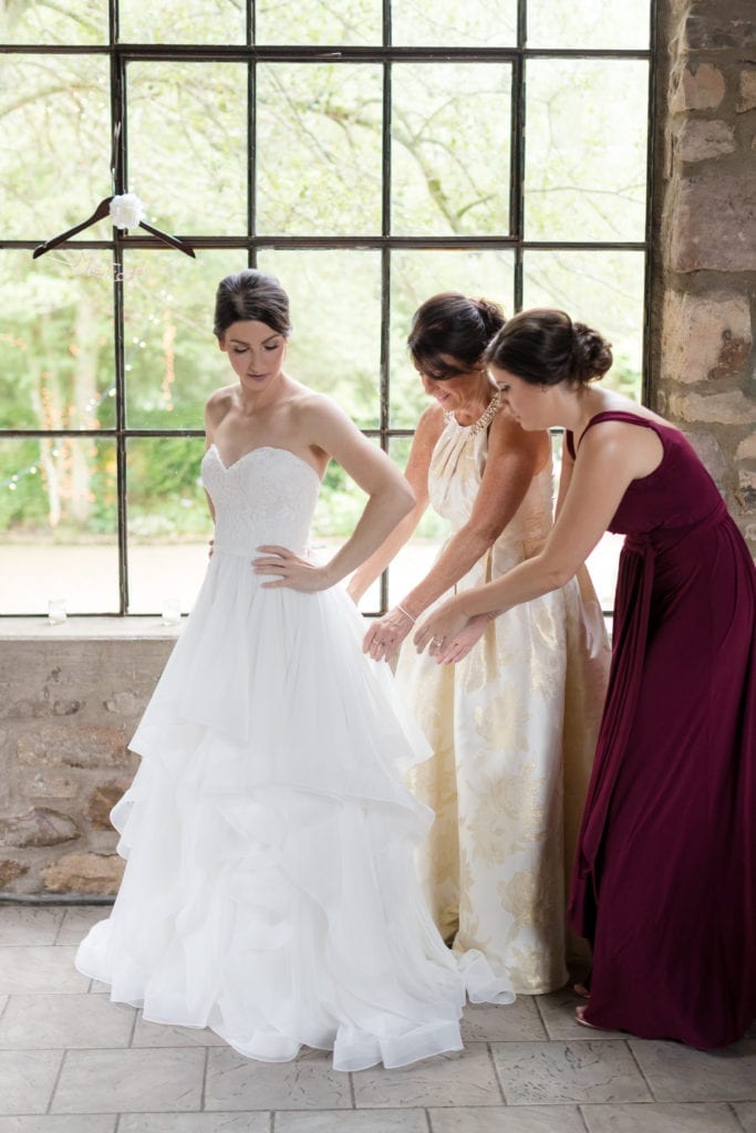 brides mother and bridesmaid helping her into her Mikaella bridal dress