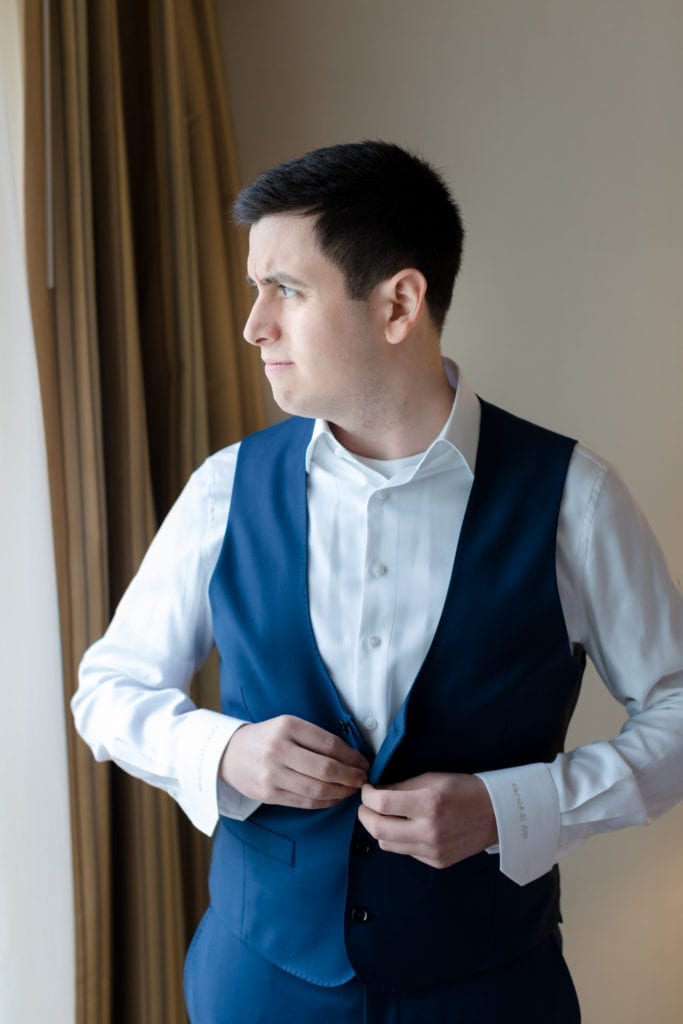 groom getting ready for his wedding day; groom buttoning vest 