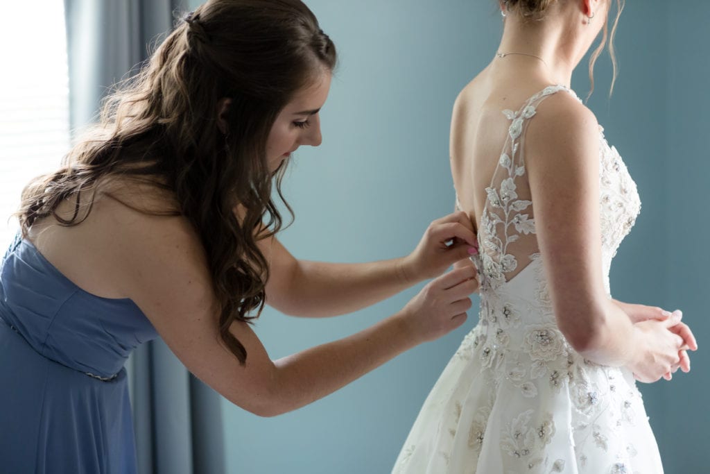 bridesmaids buttoning up wedding dress, bride getting ready