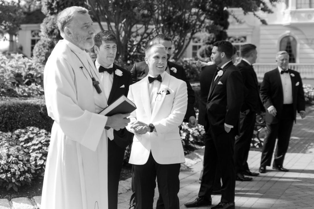 Black and white wedding photography, groom and priest