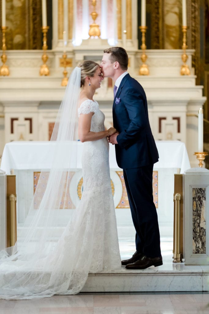groom kissing bride on the forehead at the altar