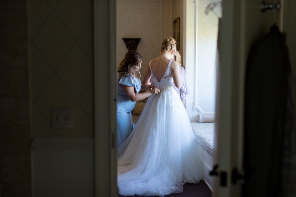 bridesmaids getting into her gown on wedding day