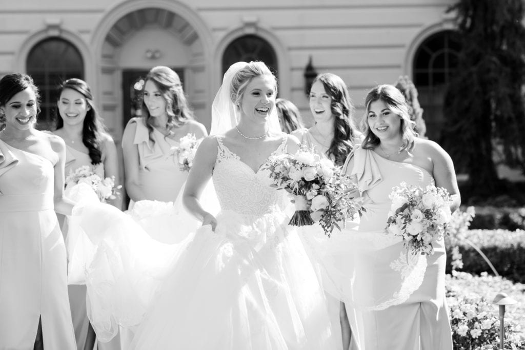 black and white photo of bride with her bridesmaids holding her dress
