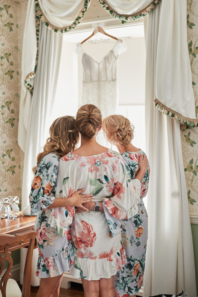 bride with maid of honor and bridesmaids looking at wedding dress in historical charming wedding venue. Photo by Vanessa Joy Photography.
