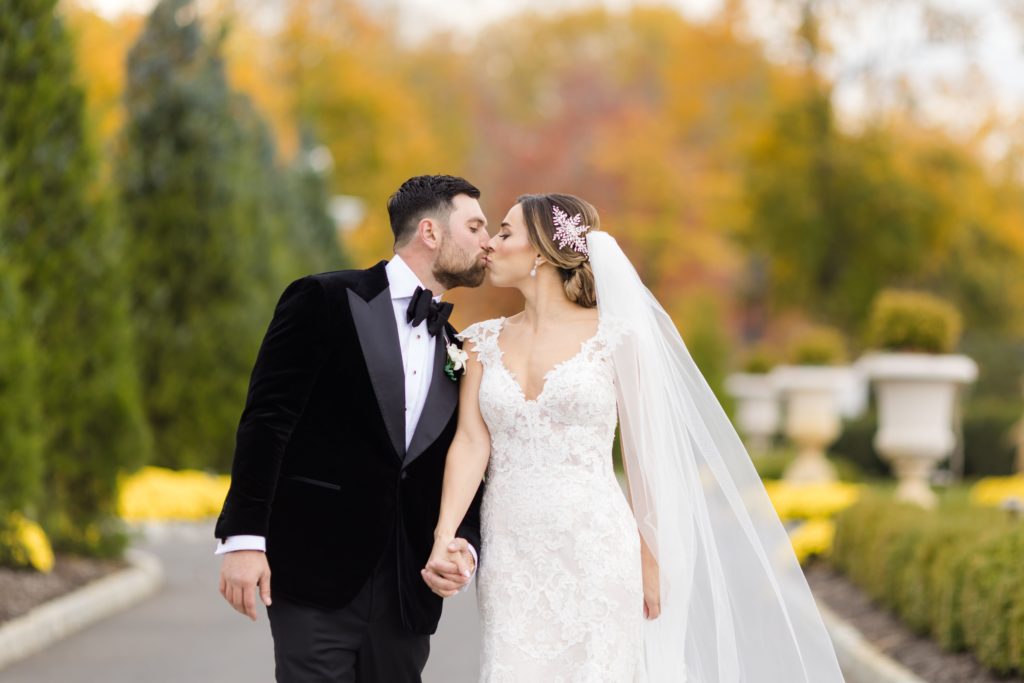 Bride and groom kiss, wedding portraits, Maggie Sottero Designs wedding gown, lace-edged veil, classic tux