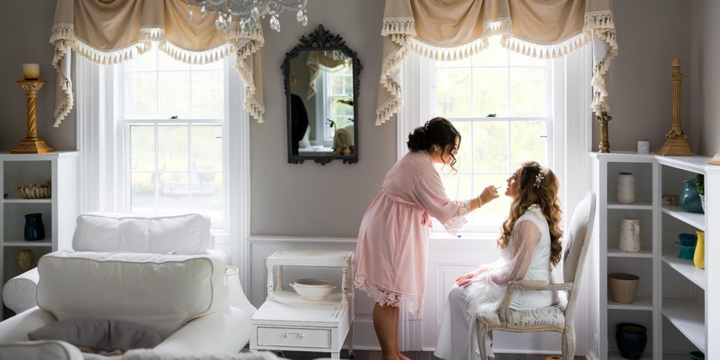 bridesmaid touching up bride's makeup on wedding day